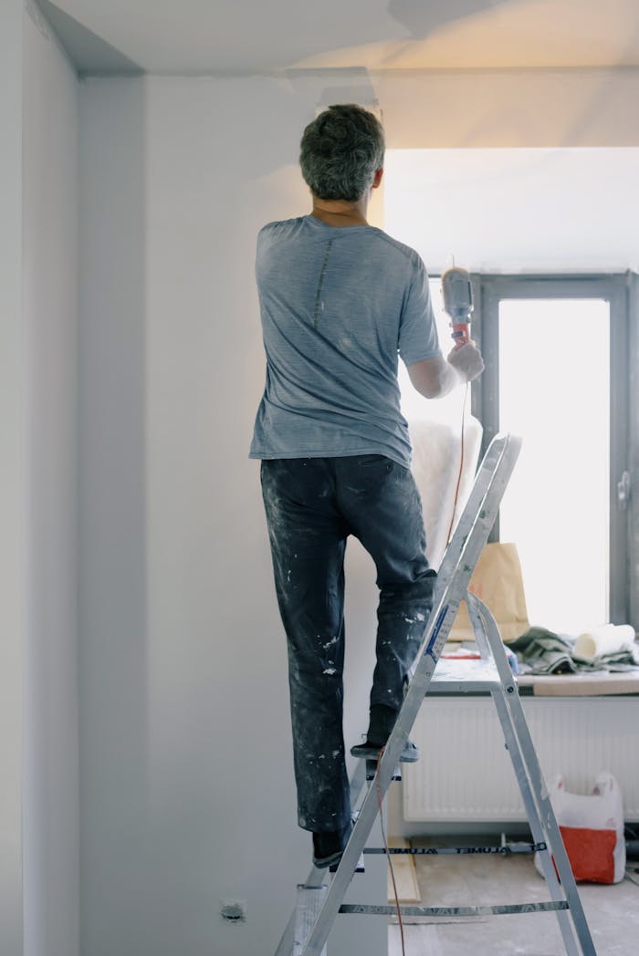 Back view full body of anonymous handyman on ladder doing renovation works in flat
